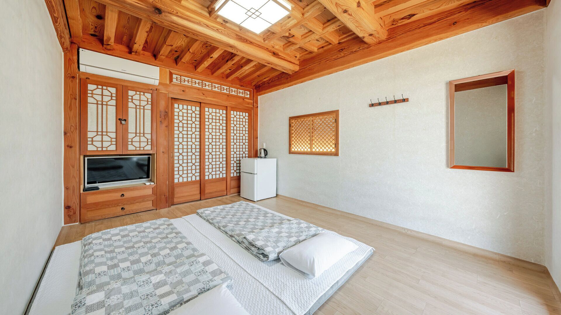 A room with a wooden ceiling, a TV, a refrigerator, a bed with a quilt, and a sliding door with a lattice design.