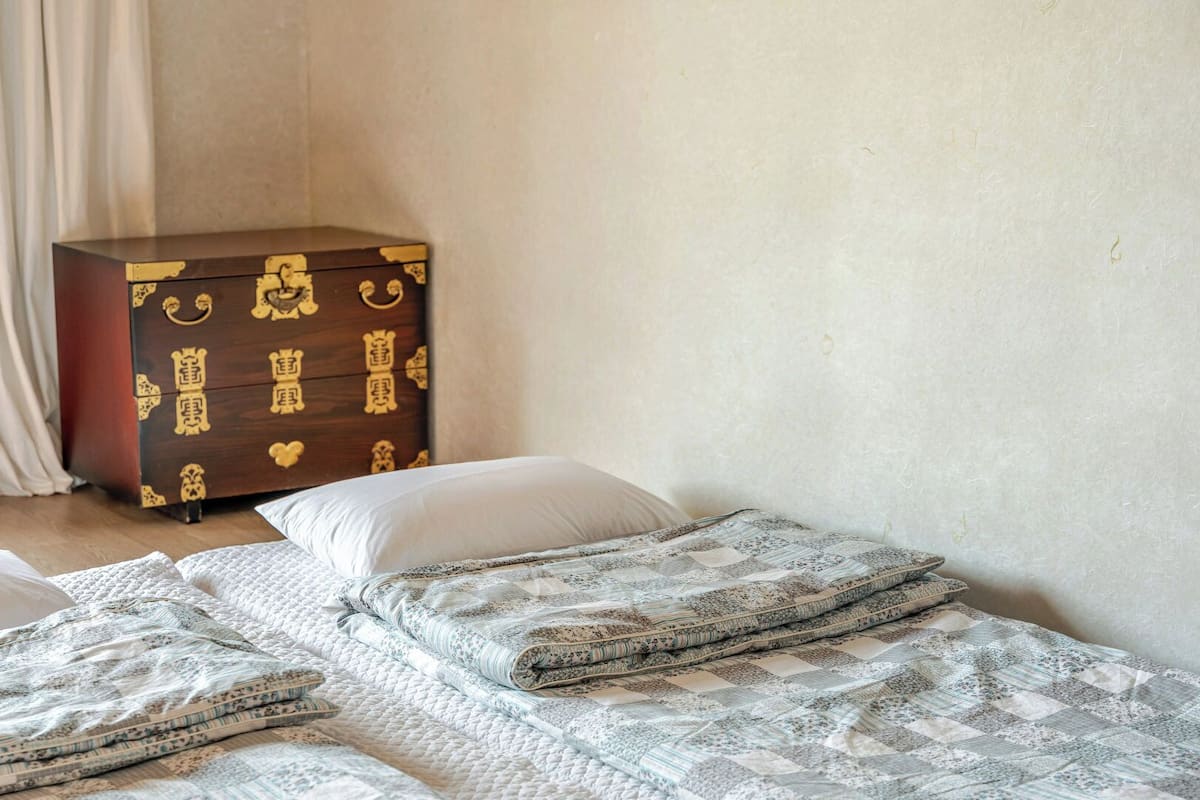 A bedroom with a bed, a pillow, a quilted blanket, and a wooden chest of drawers.