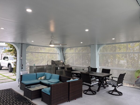 An enclosed patio area with a grill, seating, and a ceiling fan.