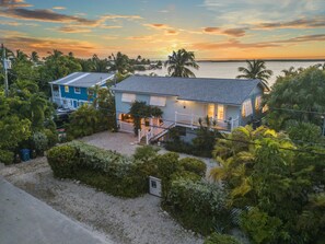 A coastal house with a balcony, surrounded by lush greenery and palm trees, overlooking the sea. - Key West Beach House with heated pool, tiki, and dock.♿︎ (Key West)