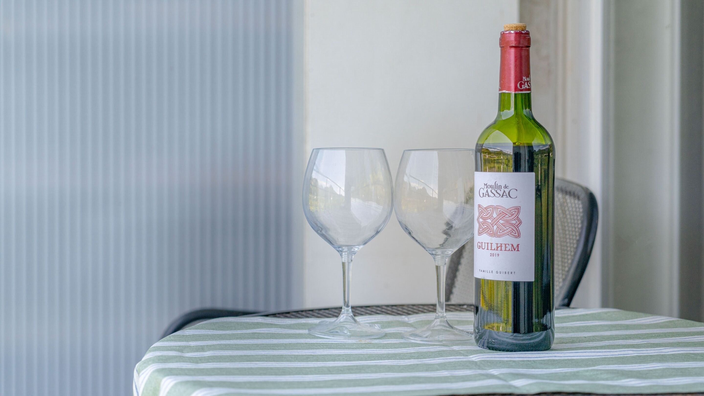 Une bouteille de vin et deux verres sur une table recouverte d’une nappe à rayures.