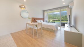 Ein modernes Schlafzimmer mit einem großen Bett, einem Schreibtisch und einem Stuhl. Ein Fenster bietet Blick auf Grünflächen und Hügel.