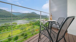 A balcony with a table, chairs, and a view of a river and mountains.