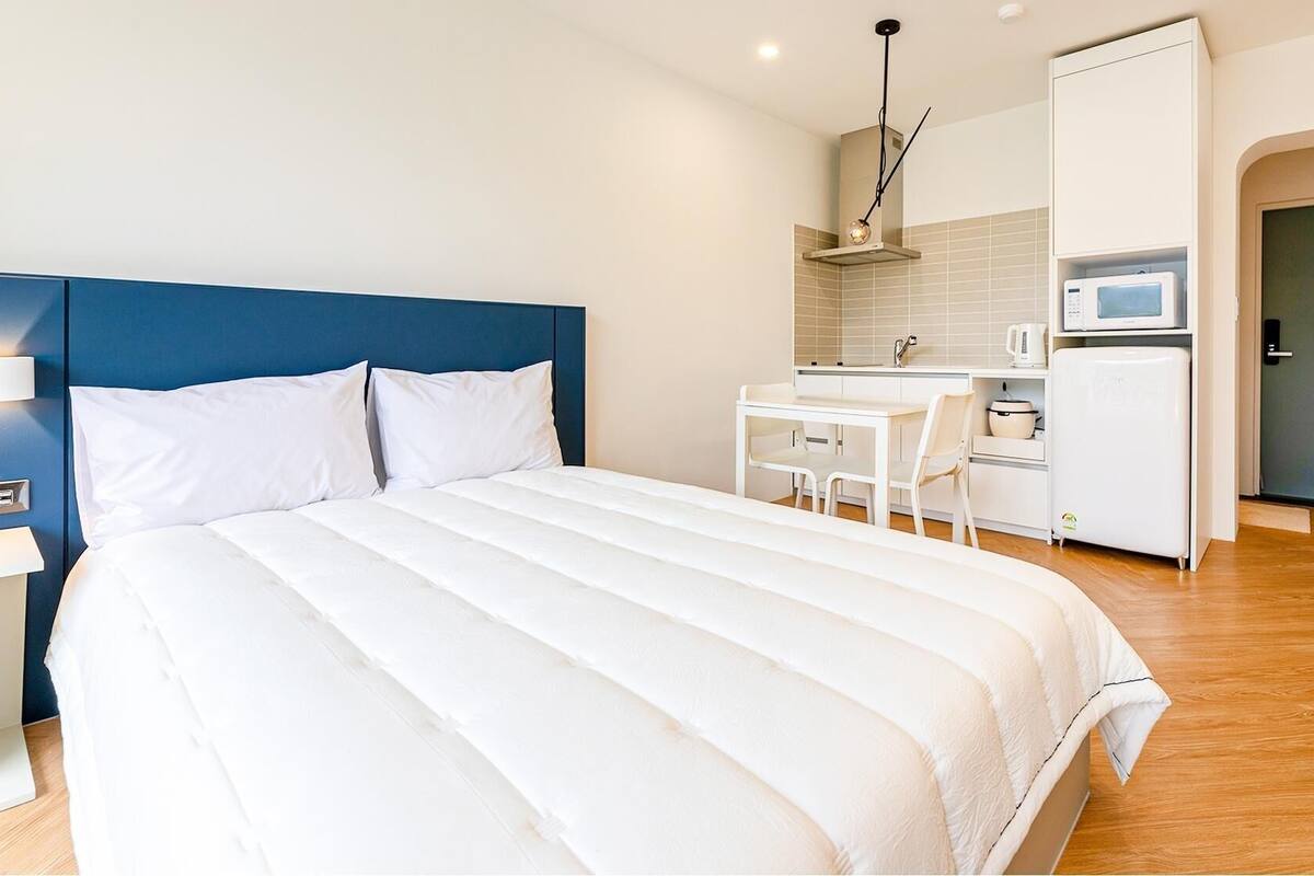 A hotel room with a bed, a desk, a microwave, and a door.