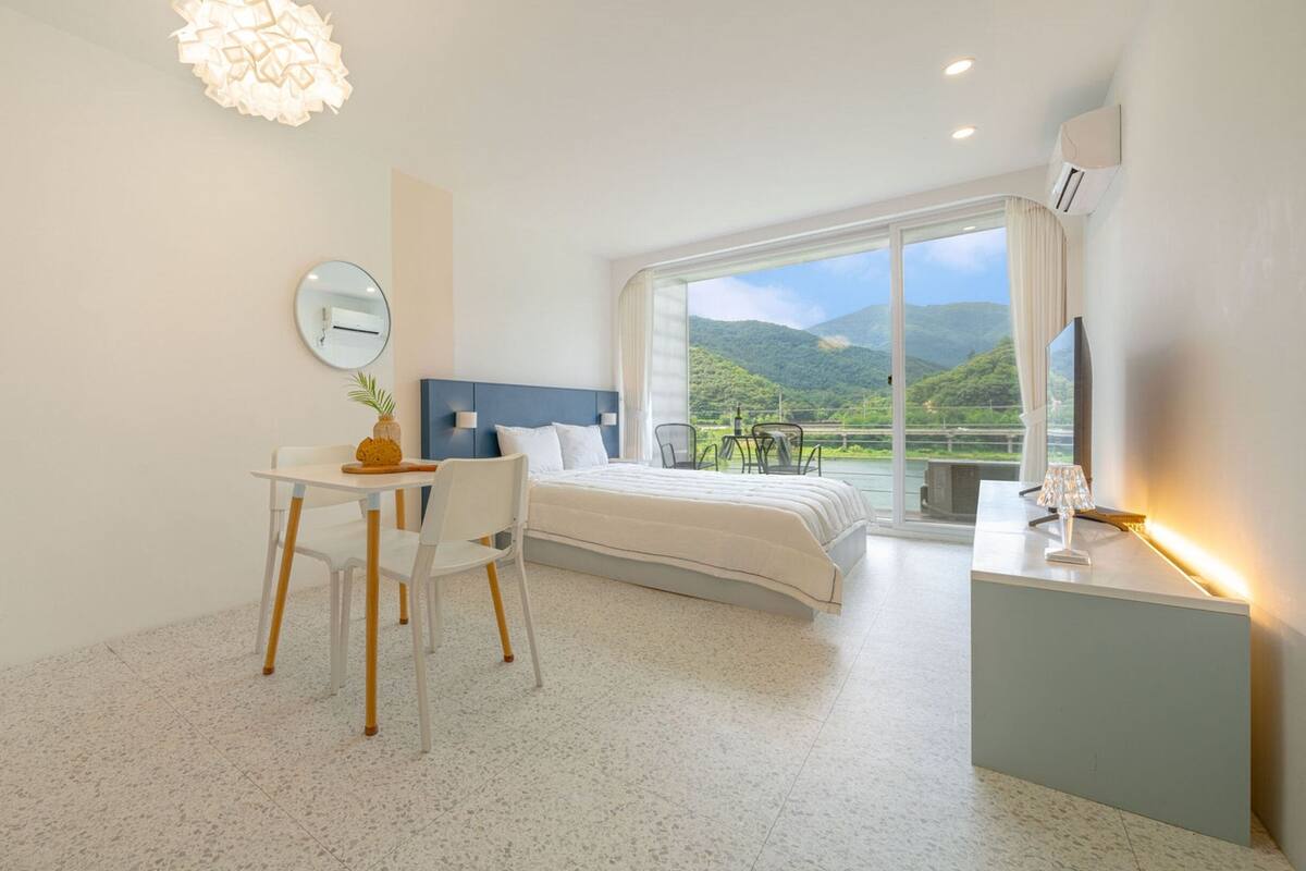 A modern hotel room with a bed, a desk, and a large window offering a scenic view.