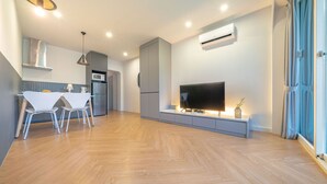 Ein modernes Wohnzimmer mit Flachbildfernseher, einem Essbereich mit weißen Stühlen und einer Küche mit Mikrowelle und Kühlschrank.
