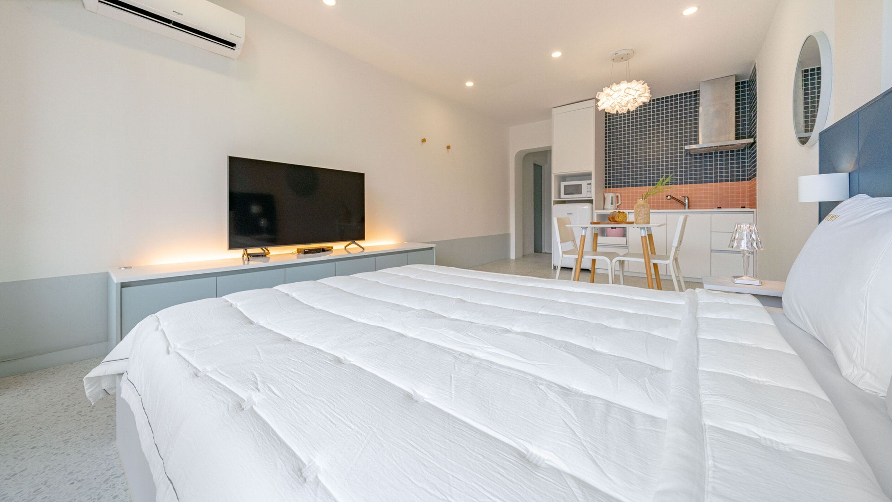 Quarto moderno com cama grande, televisão de tela plana, pequena cozinha e área de refeições.
