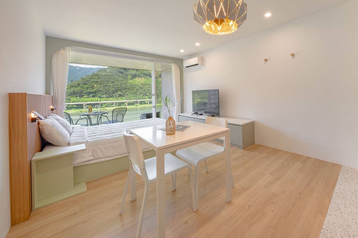 A modern room with a dining area, a TV, and a view of a green landscape.