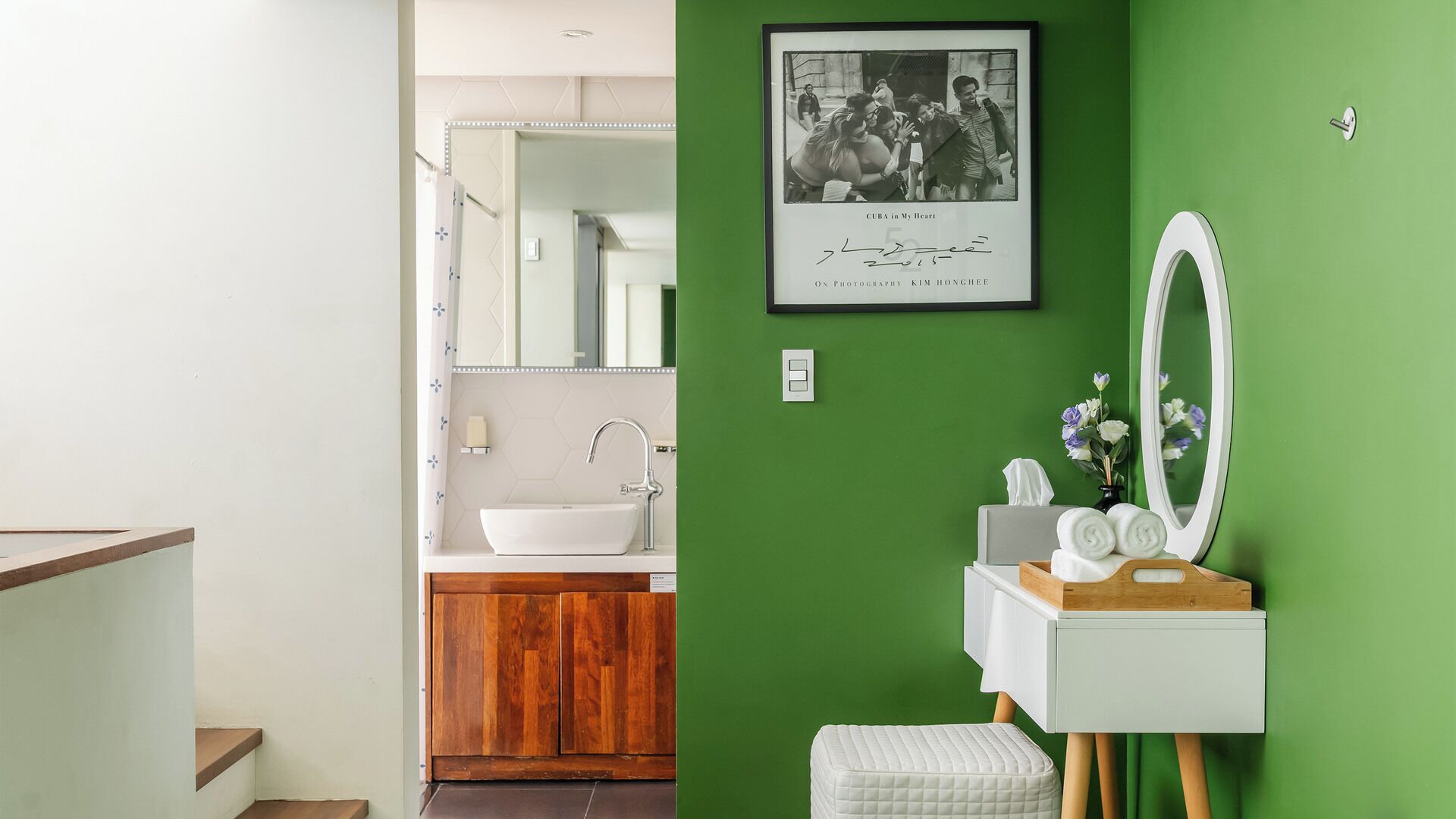 A bathroom with a green wall, a white sink, a wooden vanity, a mirror, and a framed photograph.