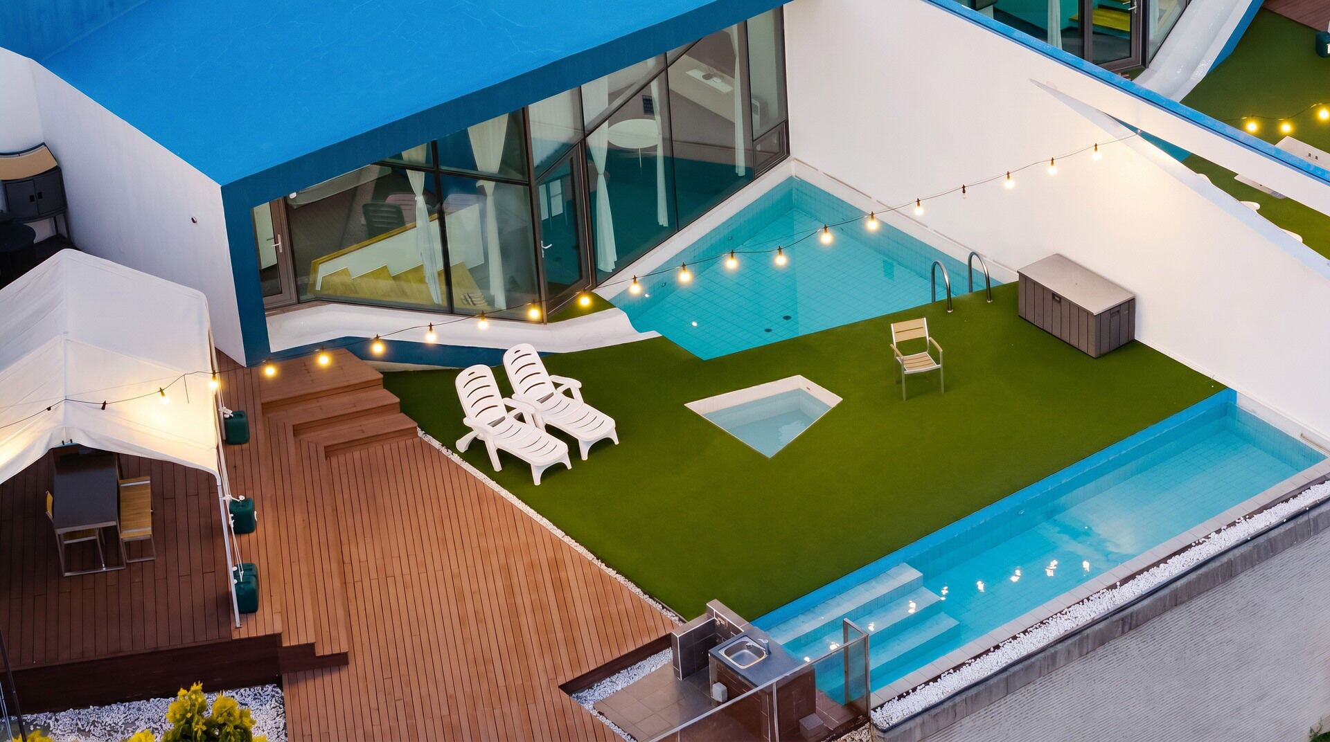 A modern outdoor pool area with a wooden deck, lounge chairs, and a small hot tub.