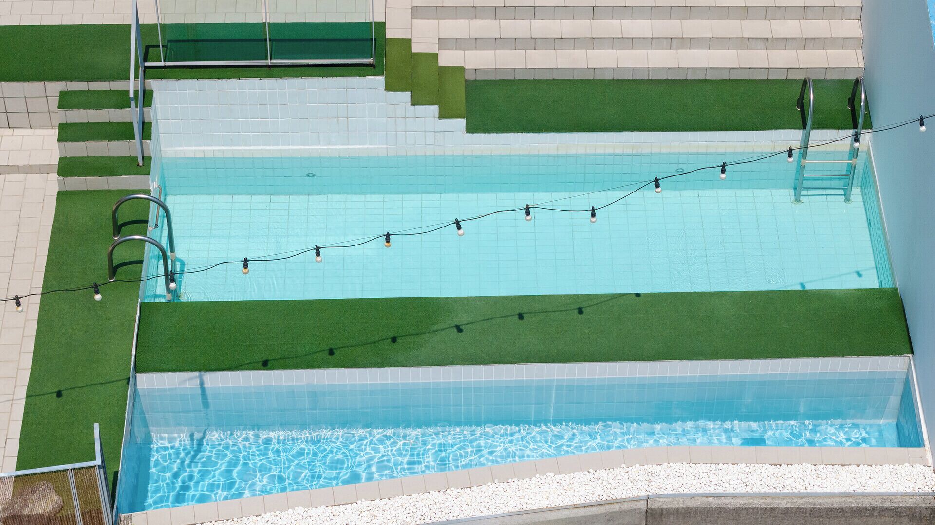 Una piscina rectangular con un borde de baldosas, una escalera y una guirnalda de luces.
