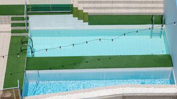 Una piscina rectangular con un borde de baldosas, una escalera y una guirnalda de luces.
