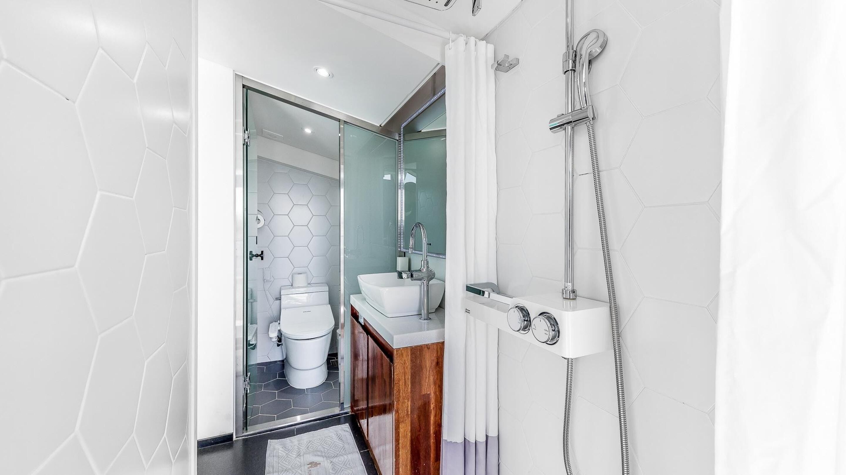 Un baño moderno con ducha de vidrio, lavamanos blanco y un inodoro.