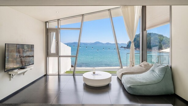 A modern room with a large window, a flat-screen TV, a round coffee table, and a light-colored sofa. - Namhae Pumda Pool Villa Pension (Namhae)