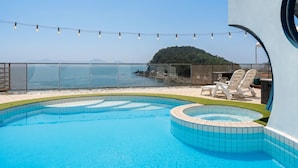A pool with a view of the sea, surrounded by lounge chairs and a deck area. - Namhae Pumda Pool Villa Pension (Namhae)
