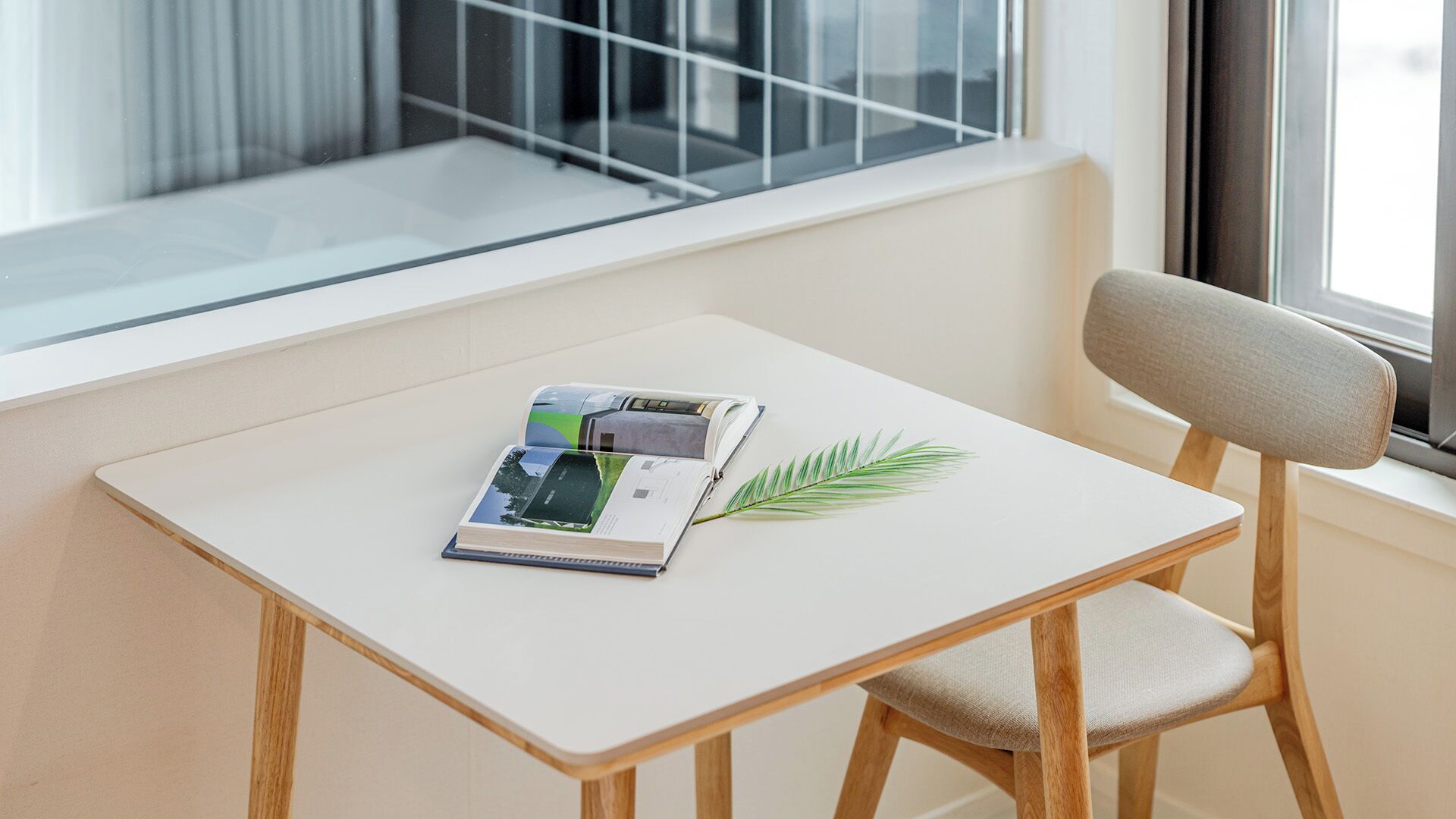 A small table with a book and a plant, a chair, and a window with a view.