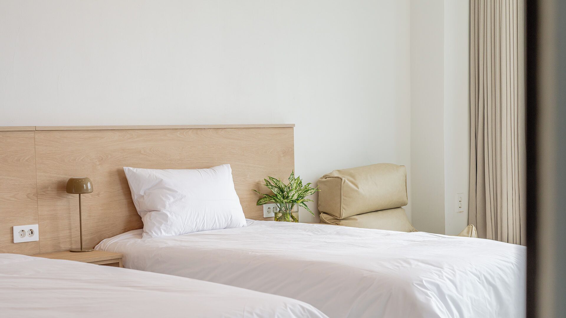 A hotel room with two beds, a bedside lamp, a plant, and a chair.