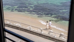 Un couple se promène sur une plage, le long d’une rambarde, avec une vue sur l’océan.