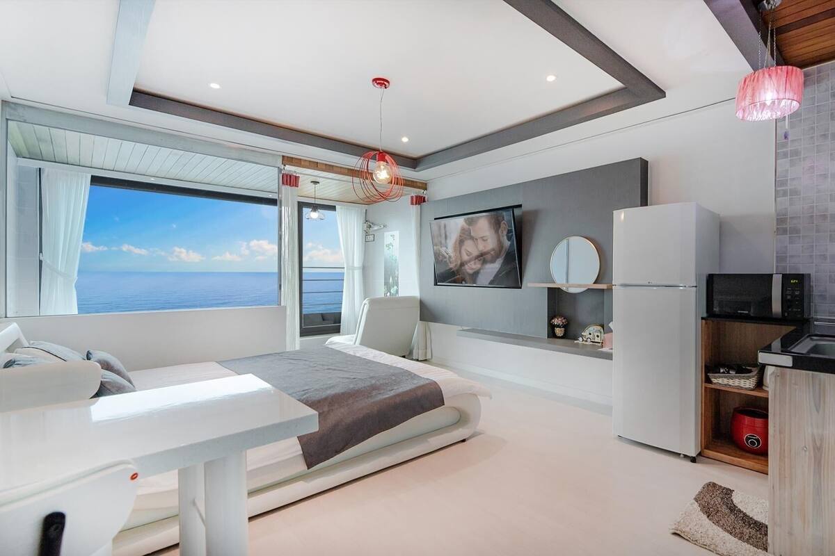 Una habitación moderna con cama, televisor, refrigerador y una zona de cocina.