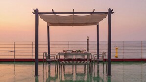 Mesa posta sob um toldo em um deck com vista para o mar.