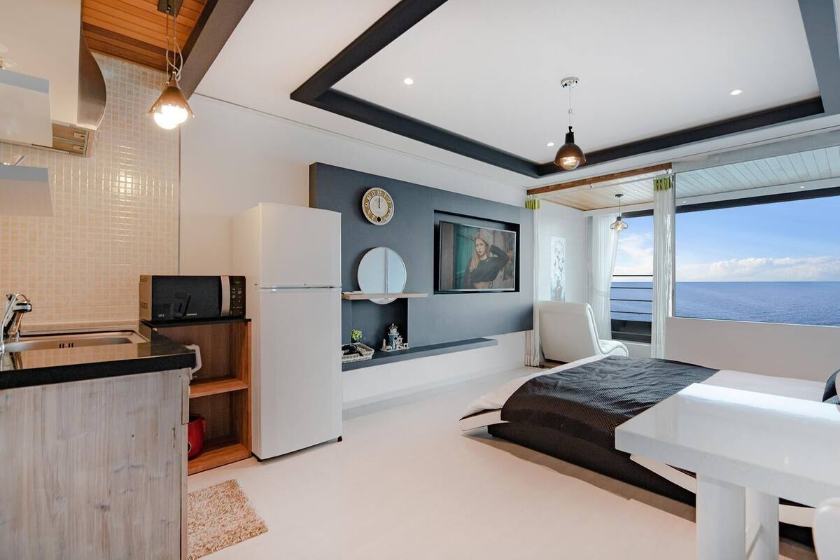 Una habitación moderna con cocina, cama, televisor y vistas al mar.