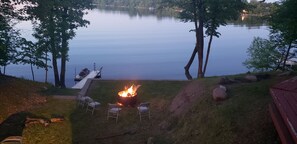 A lakeside fire pit area with chairs and a dock.