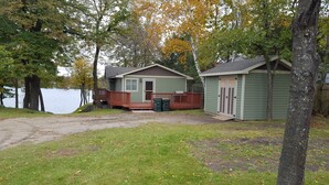 Une cabane dotée d’une terrasse et d’un petit abri de jardin, située près d’un lac.