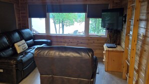 L'intérieur d'une cabine est aménagé avec un canapé en cuir, un téléviseur fixé au mur et une fenêtre donnant sur la forêt.