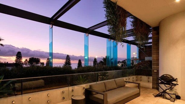 Un espace extérieur moderne, aménagé avec une balustrade en verre, un canapé, une petite table ronde et un barbecue.
