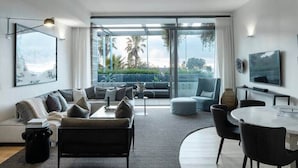 Un salon moderne comprenant un canapé, une table à manger et des chaises, un téléviseur et une grande fenêtre donnant sur un paysage verdoyant.