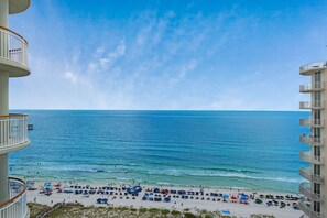 A beach with umbrellas and people, a clear sky, and a building with balconies.