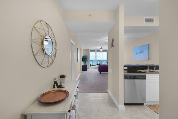 A modern kitchen with a dishwasher, a dining area with a purple sofa, and a large window overlooking the ocean.