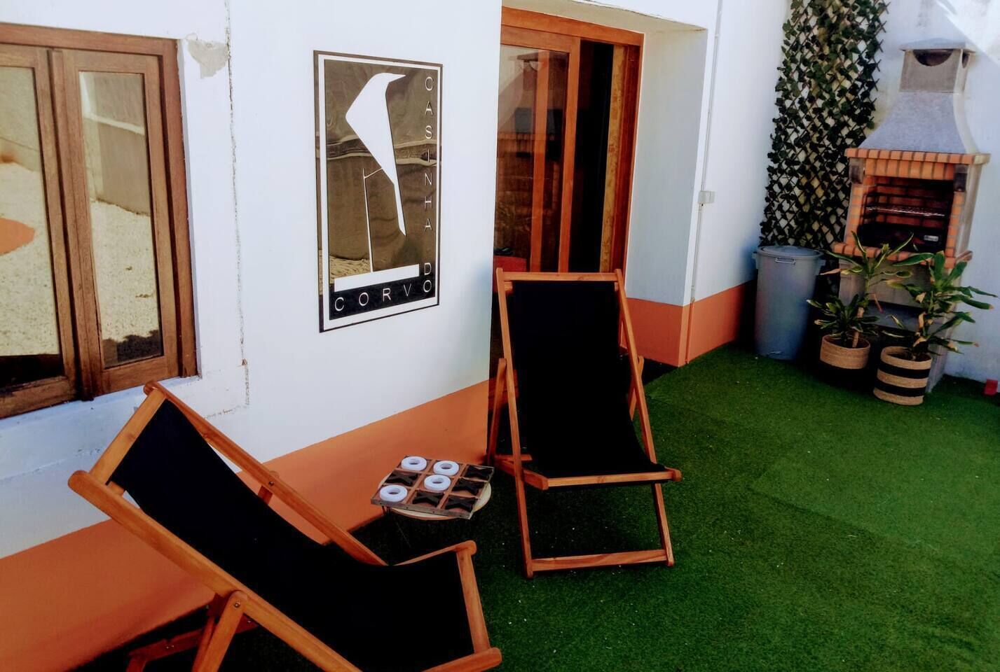 A small outdoor seating area with two wooden chairs and a table, a pizza oven, and a wall-mounted menu board.