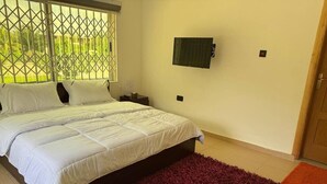 Ein Schlafzimmer mit einem Bett, einem dunkelroten Teppich, einem an der Wand montierten Fernseher und einem Fenster mit Metallgitter.