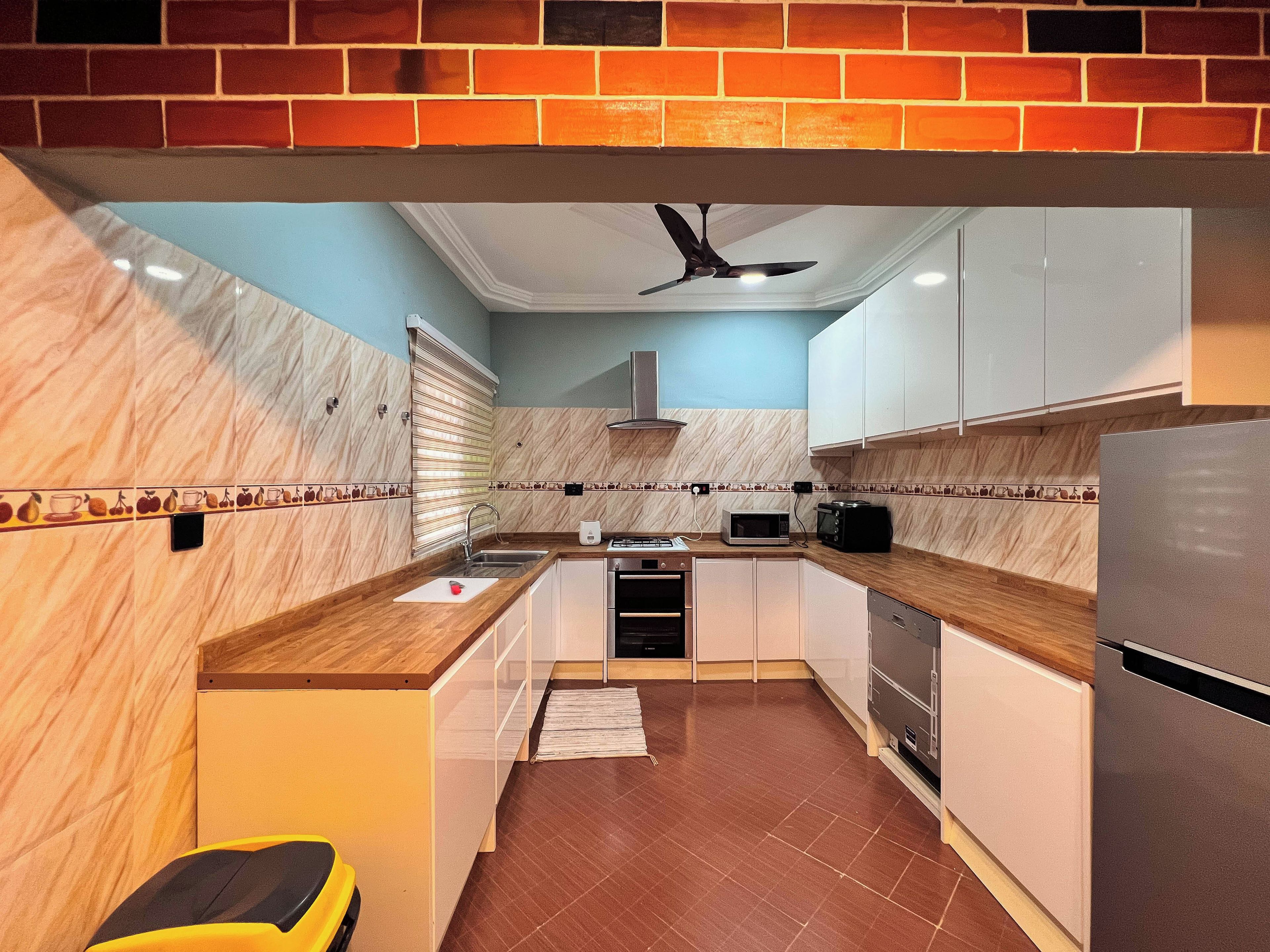 A modern kitchen with a brick accent wall, a ceiling fan, and a microwave.