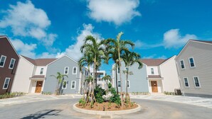 Una zona residencial con varias casas de dos pisos, un área central ajardinada con palmeras y un cielo azul despejado.