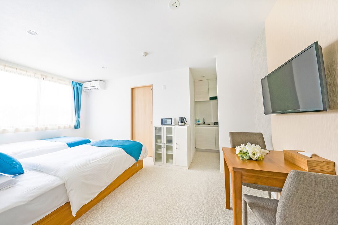 Habitación de hotel con dos camas, una mesa de comedor, un televisor y una kitchenette.