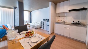 Habitación de hotel moderna con comedor, kitchenette y cama con colcha azul.