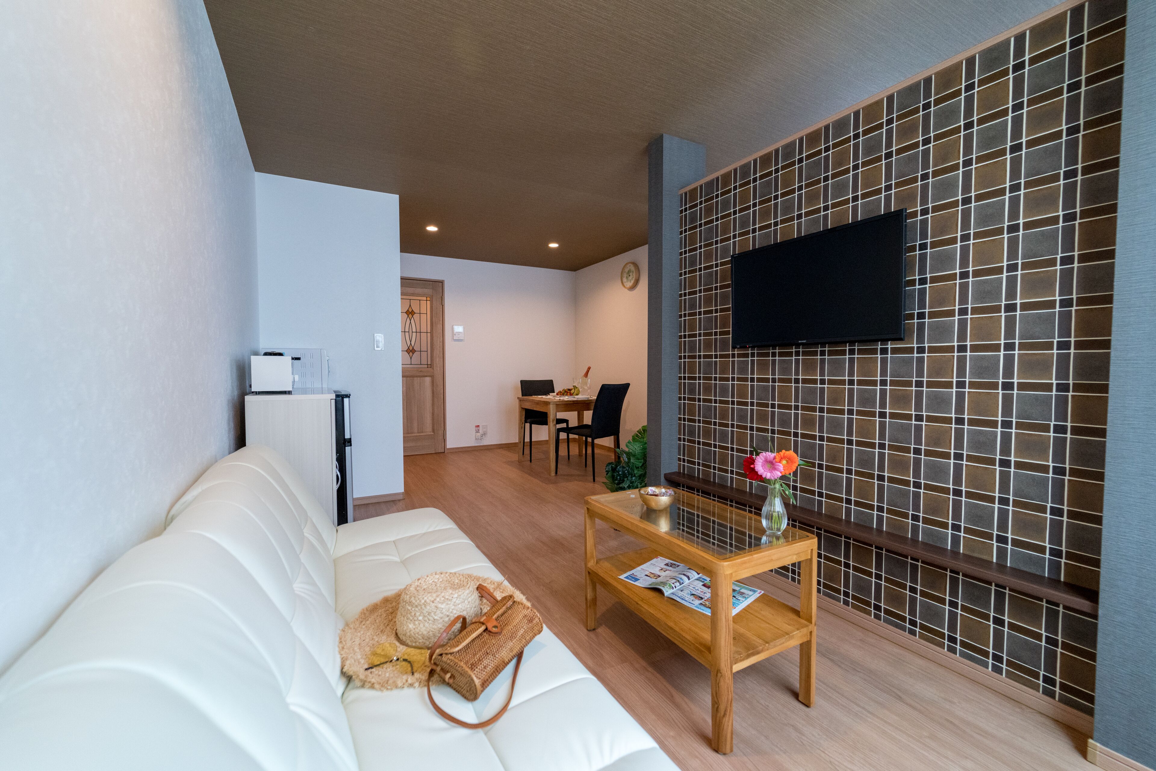 A modern living room with a white sofa, a wooden coffee table, and a TV mounted on a tiled wall.