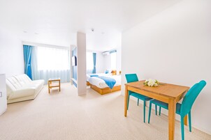 A hotel room with a bed, a wooden table with chairs, a white sofa, and a small side table.