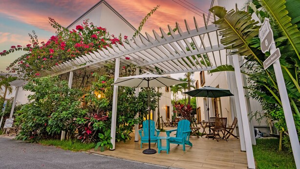 Un patio cubierto con mobiliario exterior, rodeado de abundante follaje y plantas en flor.