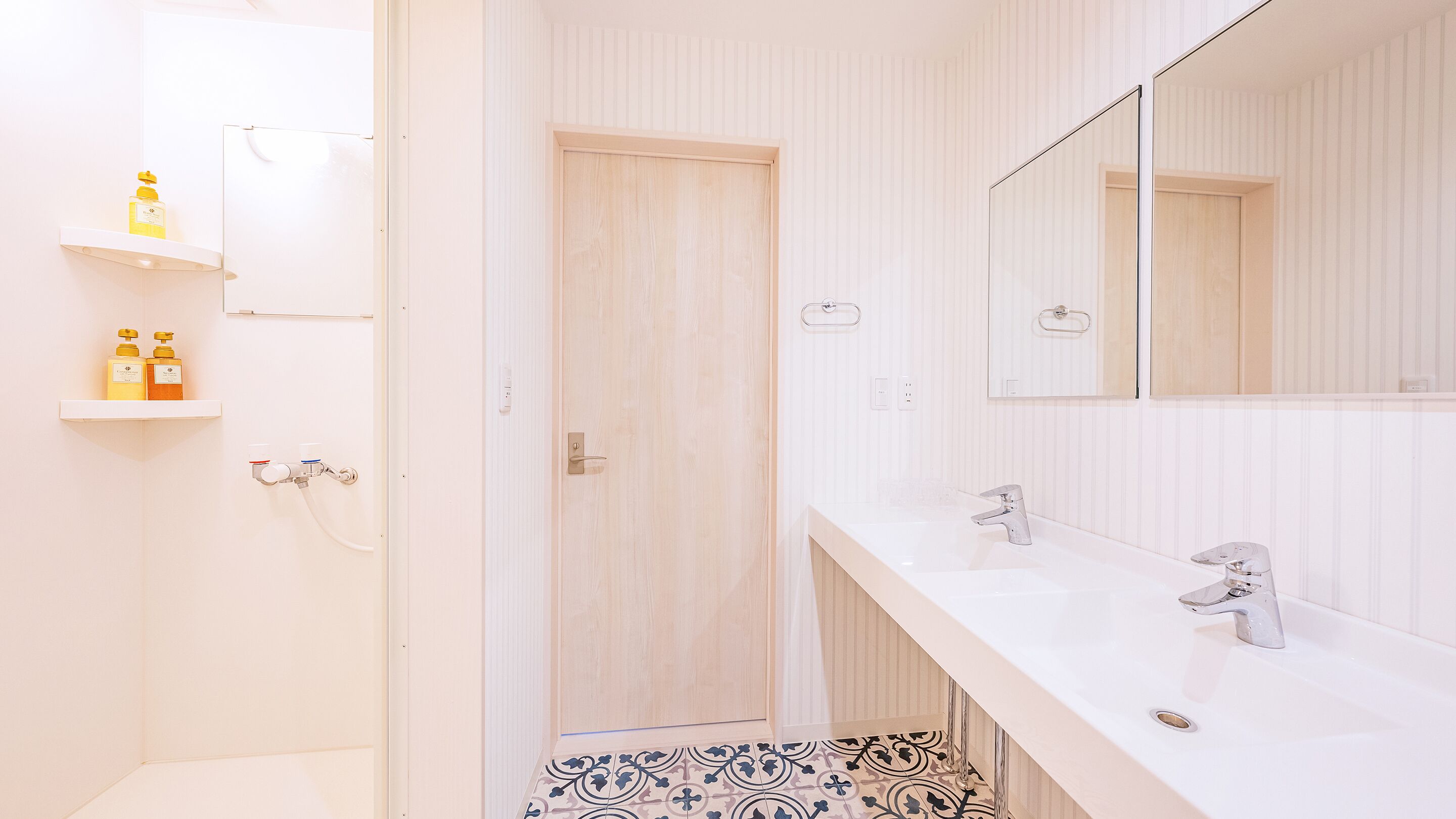 Une salle de bain avec deux lavabos, un miroir et une porte donnant sur l’espace de la douche.