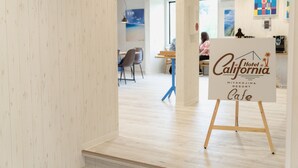 Interior de hotel con piso de madera, zona de comedor con sillas y una mesa, y un letrero que anuncia California Hotel Miyakojima Resort Cafe.