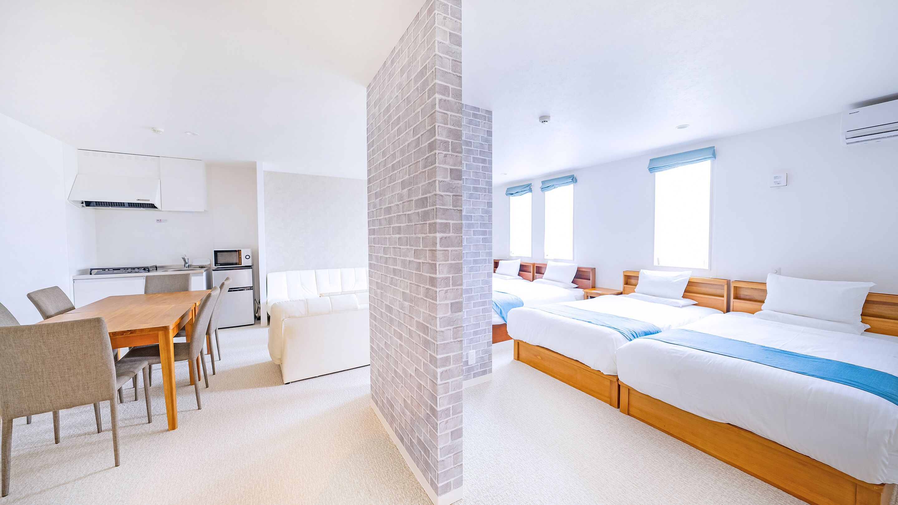 A modern hotel room with a kitchenette, a dining area, and a large bed with a blue accent.
