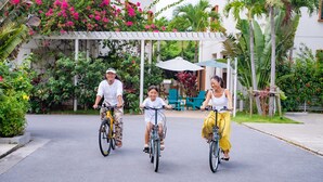 Tres personas montando en bicicleta por un camino pavimentado, con un jardín y un área de estar al aire libre al fondo.