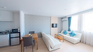 Una sala de estar moderna con sofá, una mesa de comedor y una zona de cocina con microondas y refrigerador.