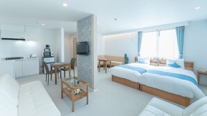 Una habitación de hotel moderna con kitchenette, una cama con detalles en azul, una zona de estar y un televisor montado en la pared.