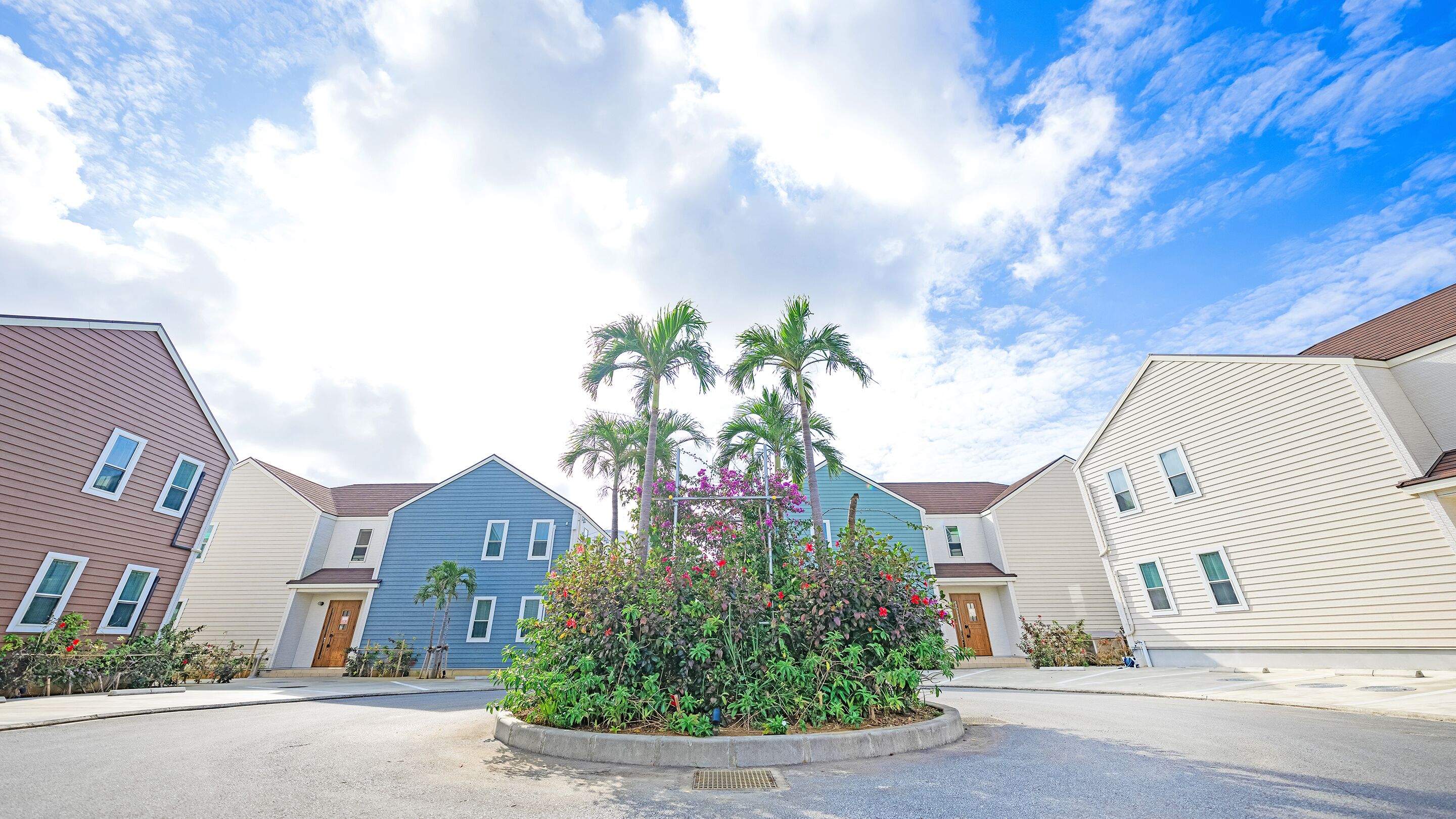 A residential area with houses, a central landscaped area with plants and flowers, and a clear sky.