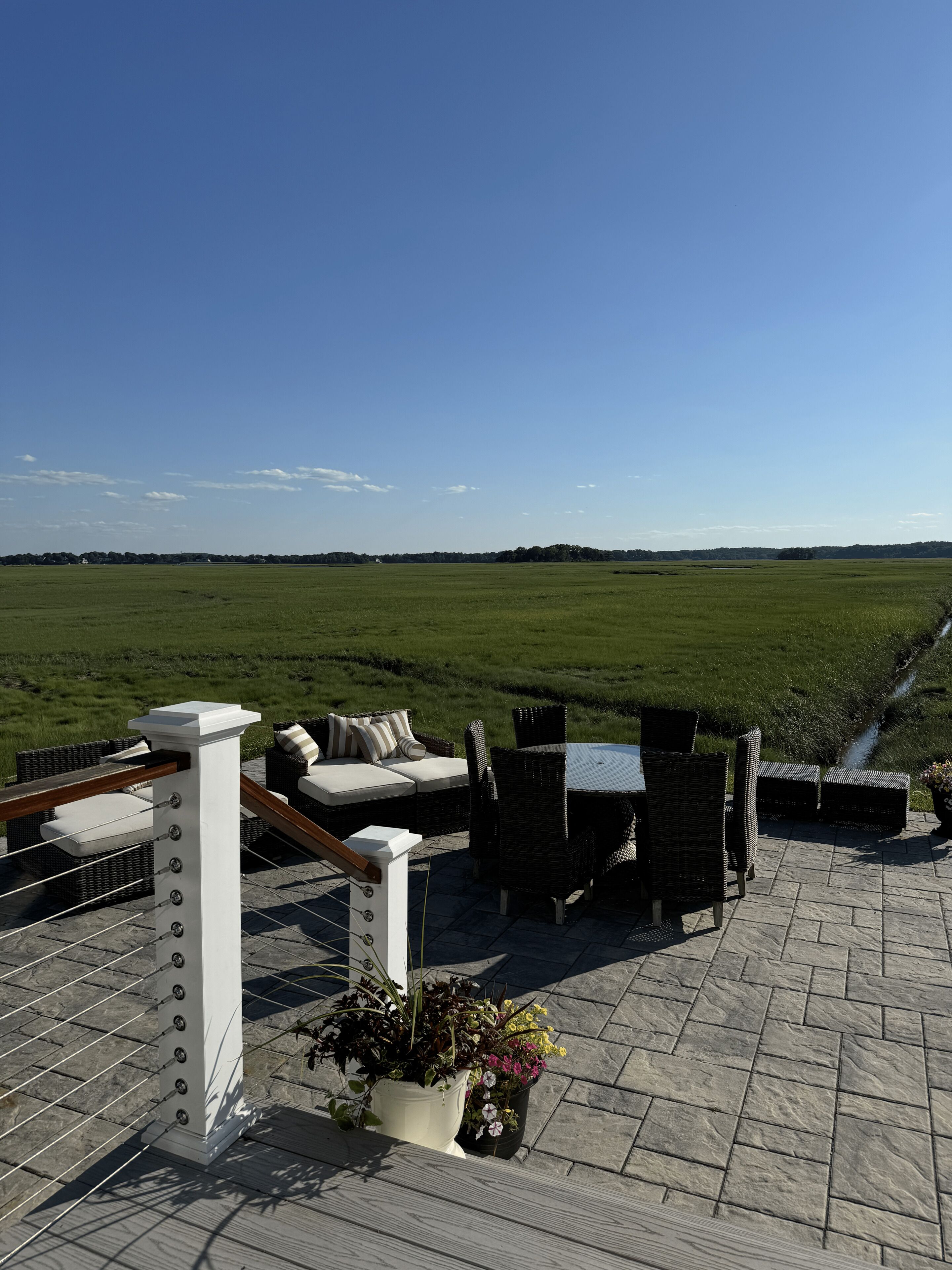 Una terraza en la azotea con mobiliario exterior, vistas a un campo verde y un cielo despejado.