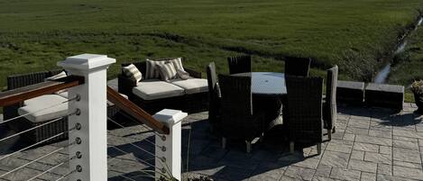 Una terraza en la azotea con mobiliario exterior, vistas a un campo verde y un cielo despejado.